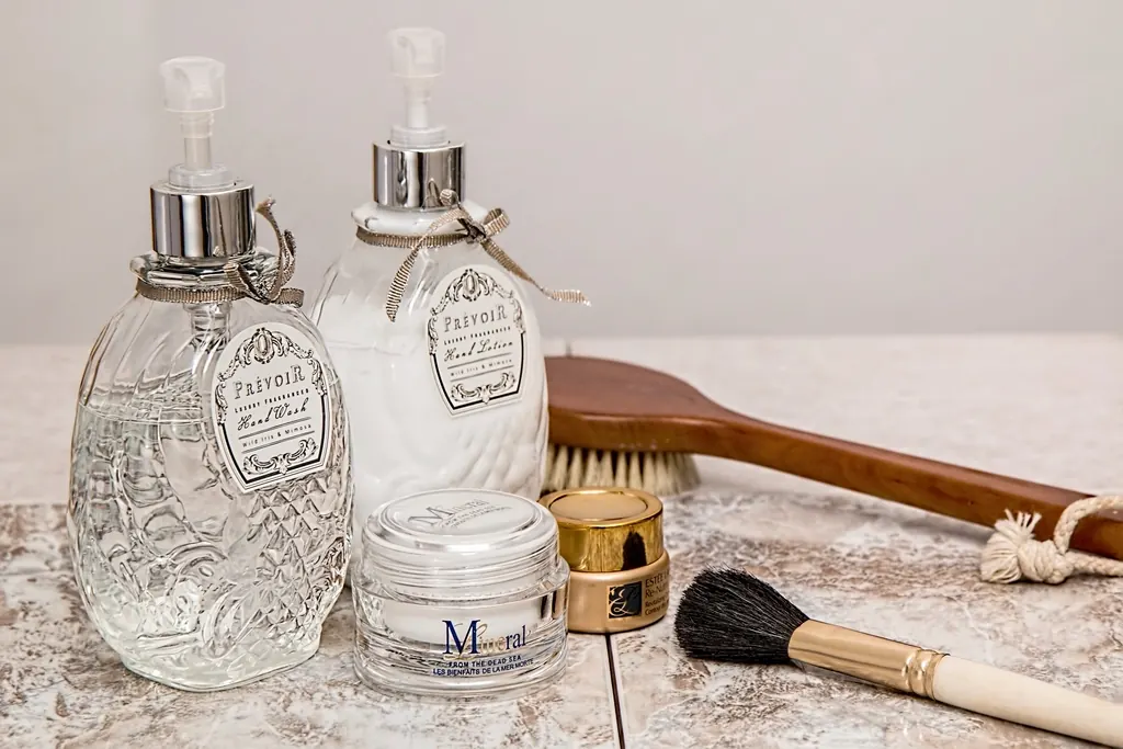 Glass skincare bottles, a jar of cream and a facial brush on marble