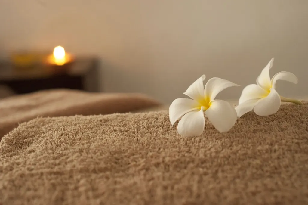 A folded spa towel with white plumeria flowers and a candle